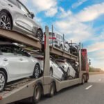 Car carrier truck transporting multiple vehicles on highway at sunset.