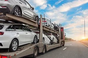 Car carrier truck transporting multiple vehicles on highway at sunset.