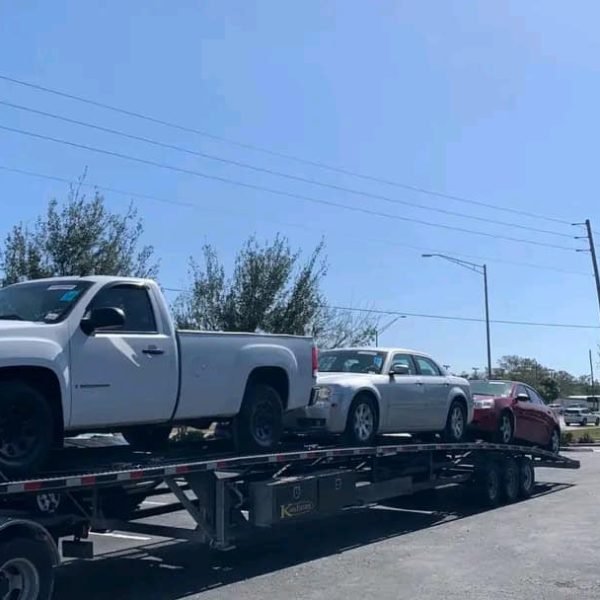 White pickup truck on a car transport trailer at a parking lot.